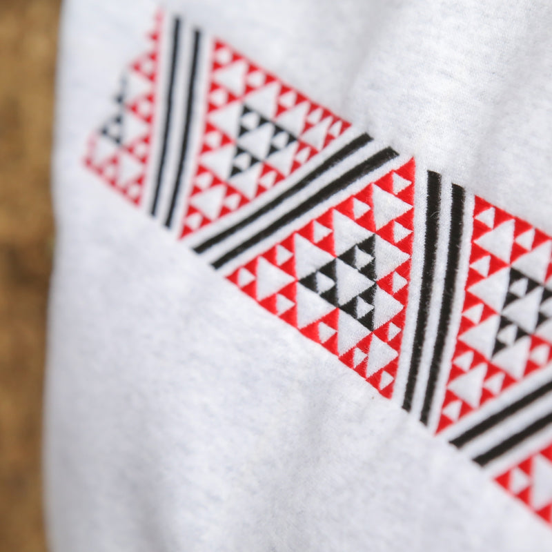 Close up of White women's crew with red and black embroidered Maori taniko design.