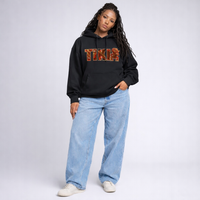 Female model wearing black Cravass AHI Tiki hoodie with red tiki-inspired graphic lettering, styled as contemporary streetwear