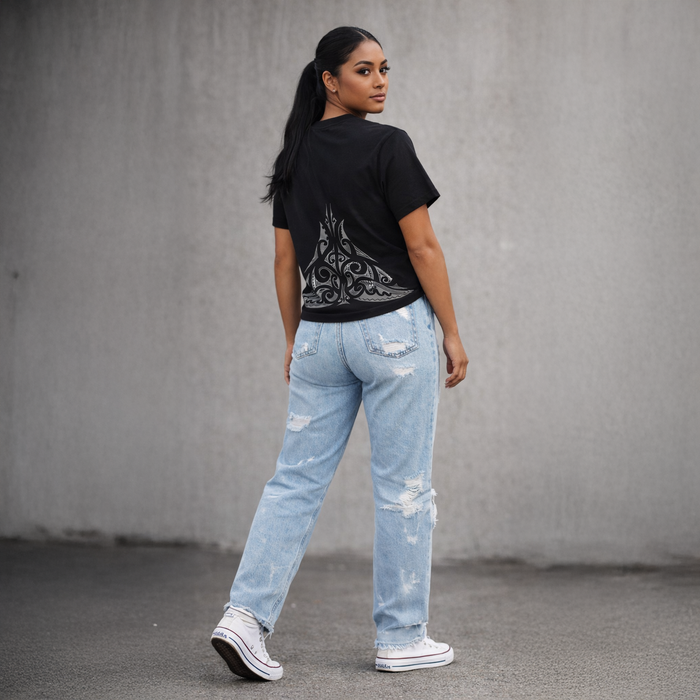 A woman wearing a black t-shirt with a design and light blue jeans against a grey background. Maori streetwear by cravass