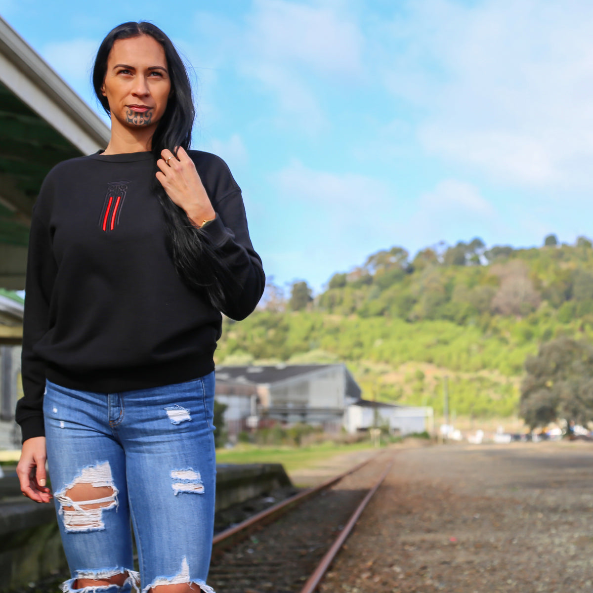 Women's black crew jersey with a black and red Maori moko kauae design. outside gisborne railway station nz