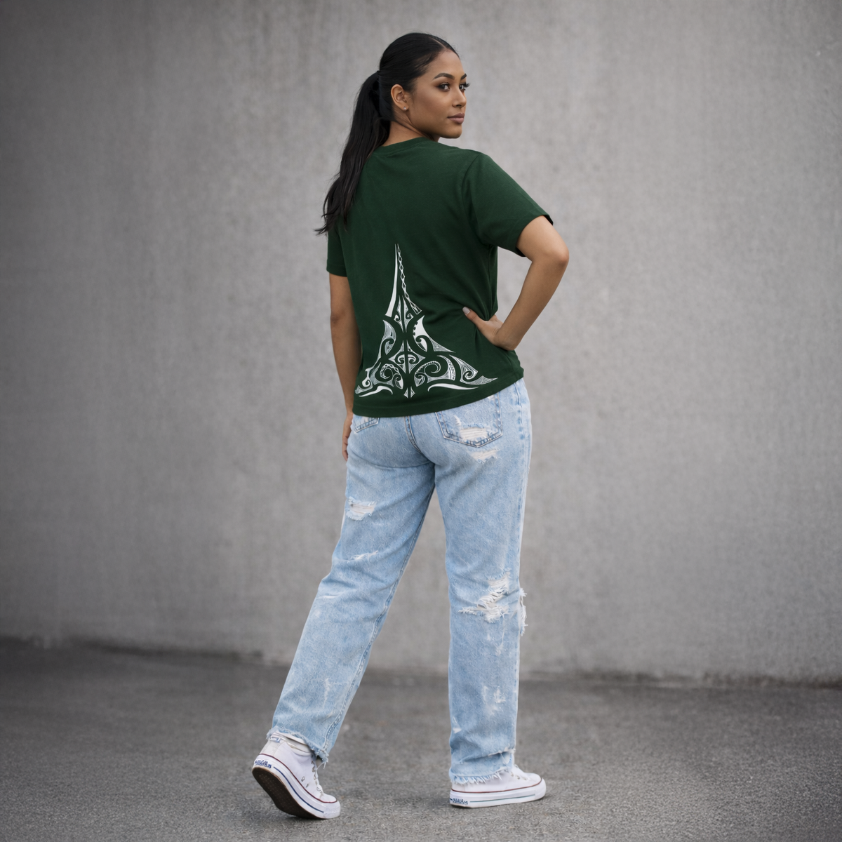 Person wearing a green t-shirt with a design on the back and light blue jeans against a gray background