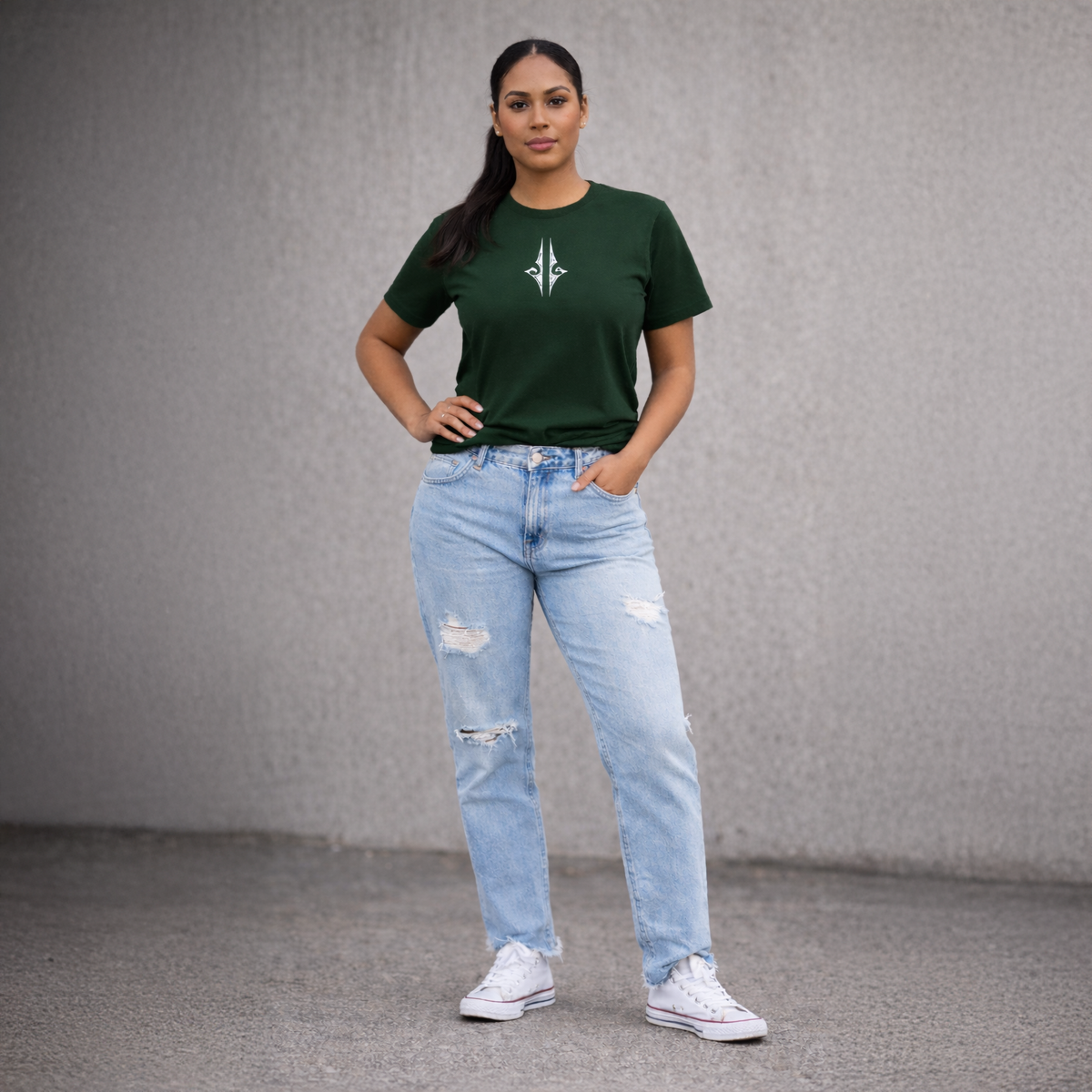 A woman wearing a green t-shirt with a logo and light blue jeans against a grey background. Streetwear by Cravass.