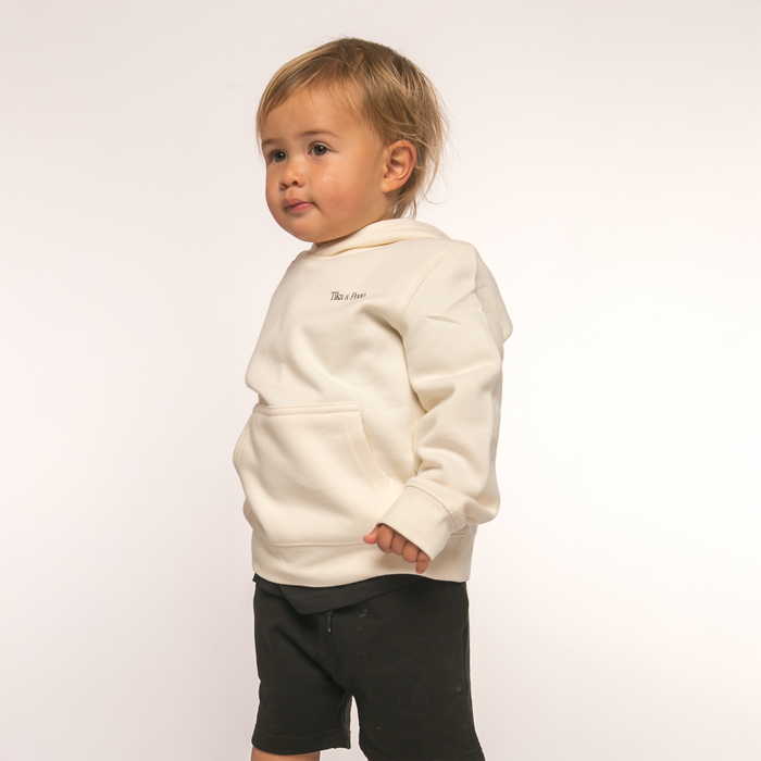 Baby wearing hoody. Front view of Tika & Pono Kids Hoody in white, featuring 'Tika & Pono' text