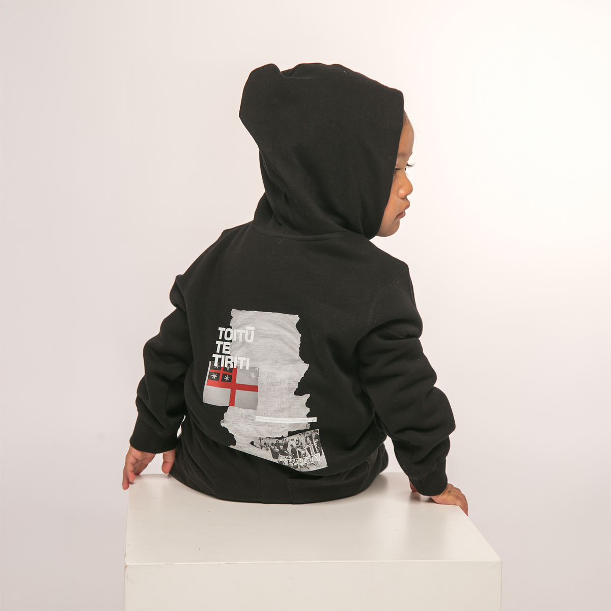 Back view of Te Kara Toi Tu Tiriti Kids Hoody in Black, showcasing the cultural design.