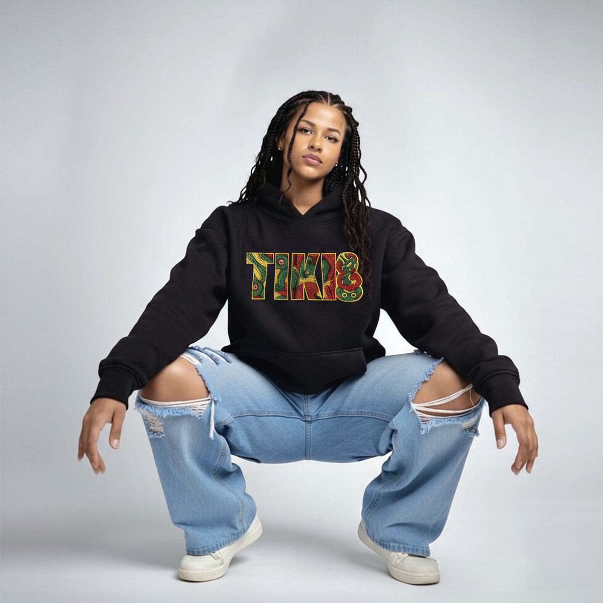 Black Cravass TIKI hoodie worn by model, featuring bold Māori-inspired TIKI graphic, styled with ripped blue jeans in studio setting