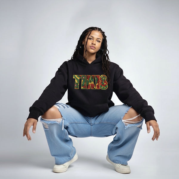 Black Cravass TIKI hoodie worn by model, featuring bold Māori-inspired TIKI graphic, styled with ripped blue jeans in studio setting