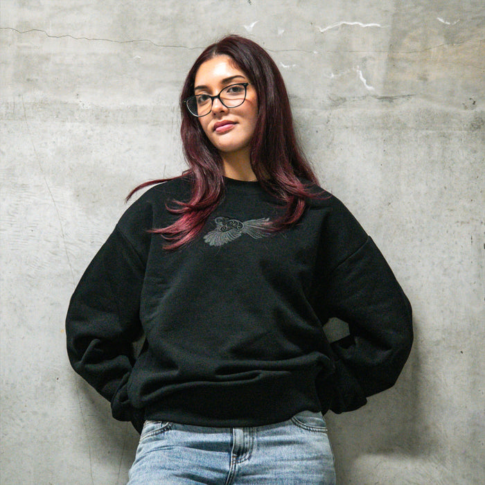 Woman wearing Cravass Pīwakawaka Black Women's Crew with detailed black-on-black embroidered native bird artwork