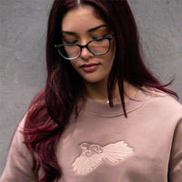 Close-up of woman wearing Pīwakawaka Hazy Pink Women's Crew with detailed embroidery by Cravass