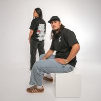 Two people wearing black t-shirts with NZ Maori graphic designs on a white background
