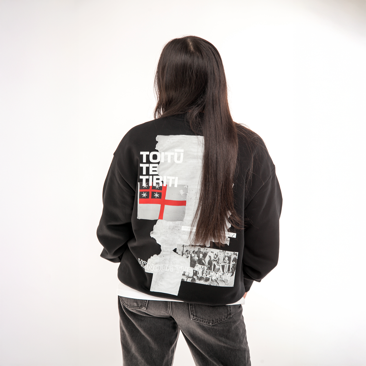 Model wearing a black sweatshirt with graphic designs and text on the back, standing against a white background.