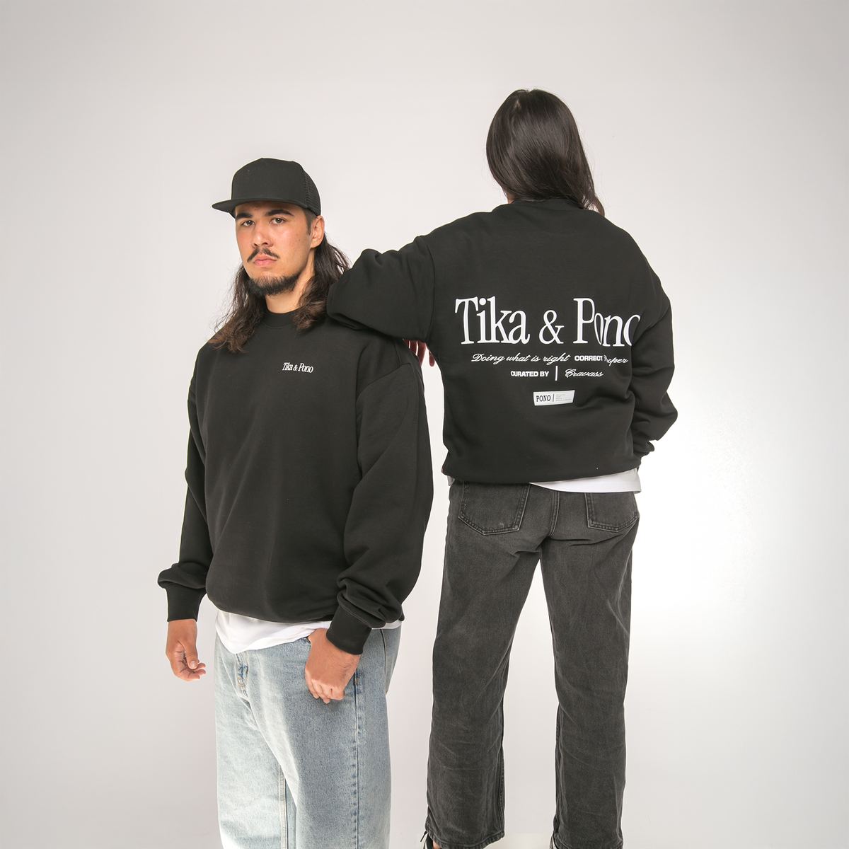 Two people wearing black sweatshirts with 'Tika & Pono' branding, one facing forward and the other showing the back.