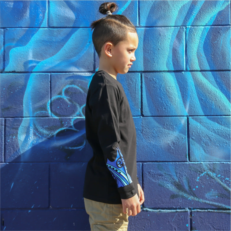 Young boy wearing black long sleeve tshirt with blue maori design on the forearm form cravass clothing. Side