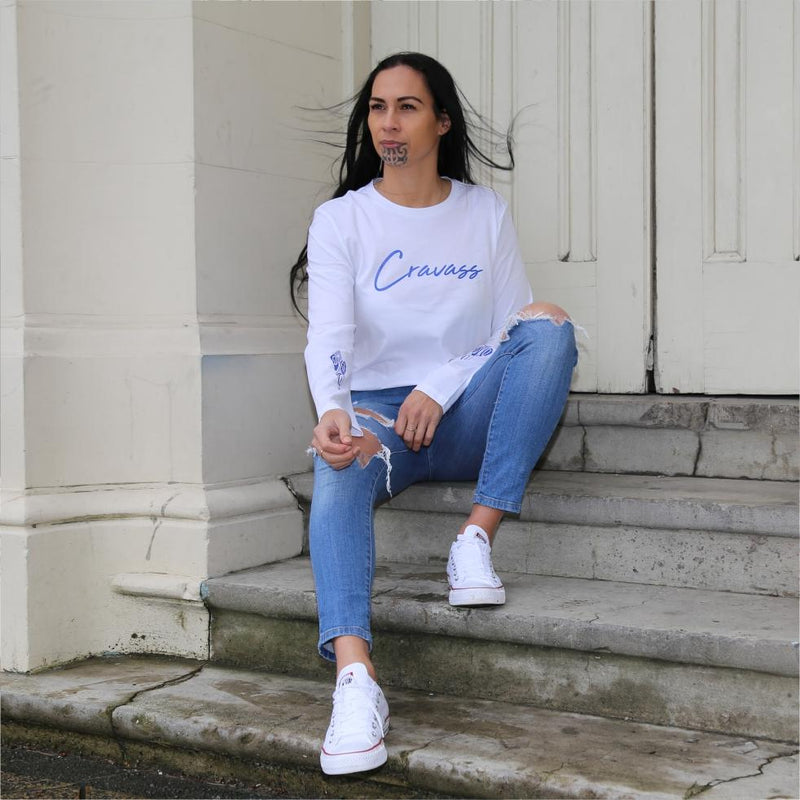 Model sitting on stairs wearing a white long sleeve tshirt with maori design.