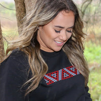 Black women's crew with red and white embroidered Maori taniko design.