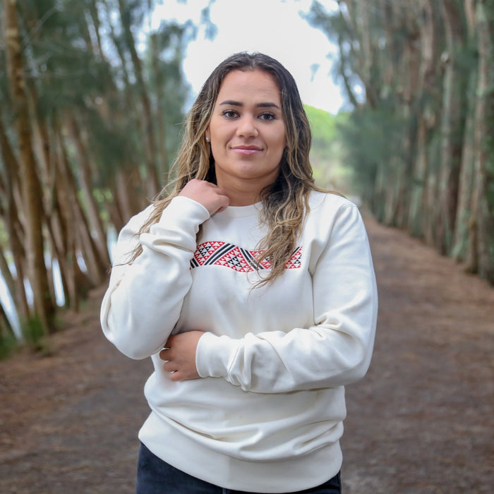 Ecru women's crew with red and black embroidered Maori taniko design.