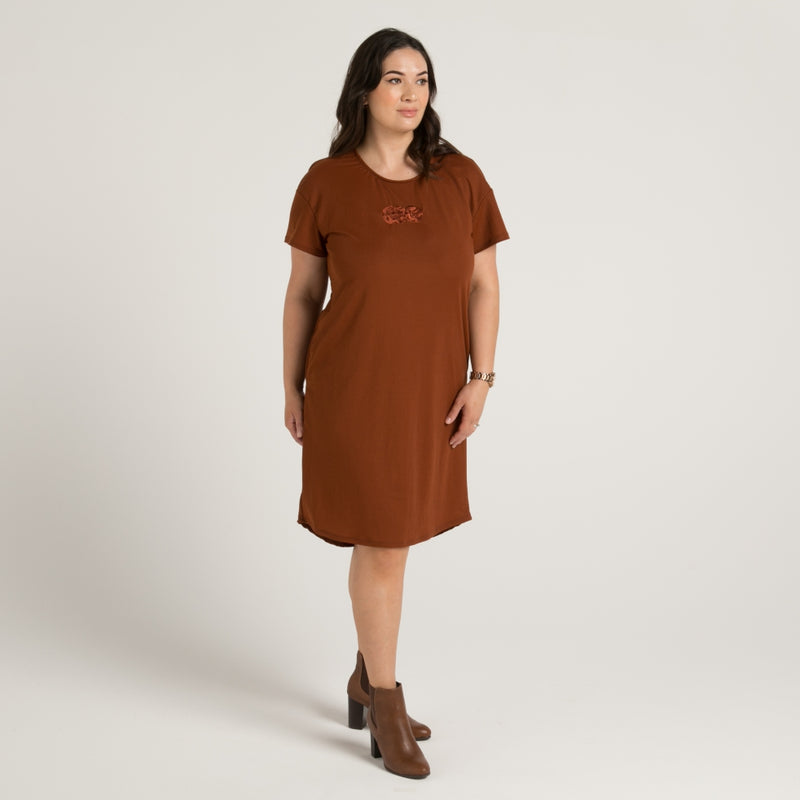 Women's brown dress with stunning embroidered maori tiki, dress has pockets and drop hem front and rear. Made in Aotearoa Tauranga New Zealand.  