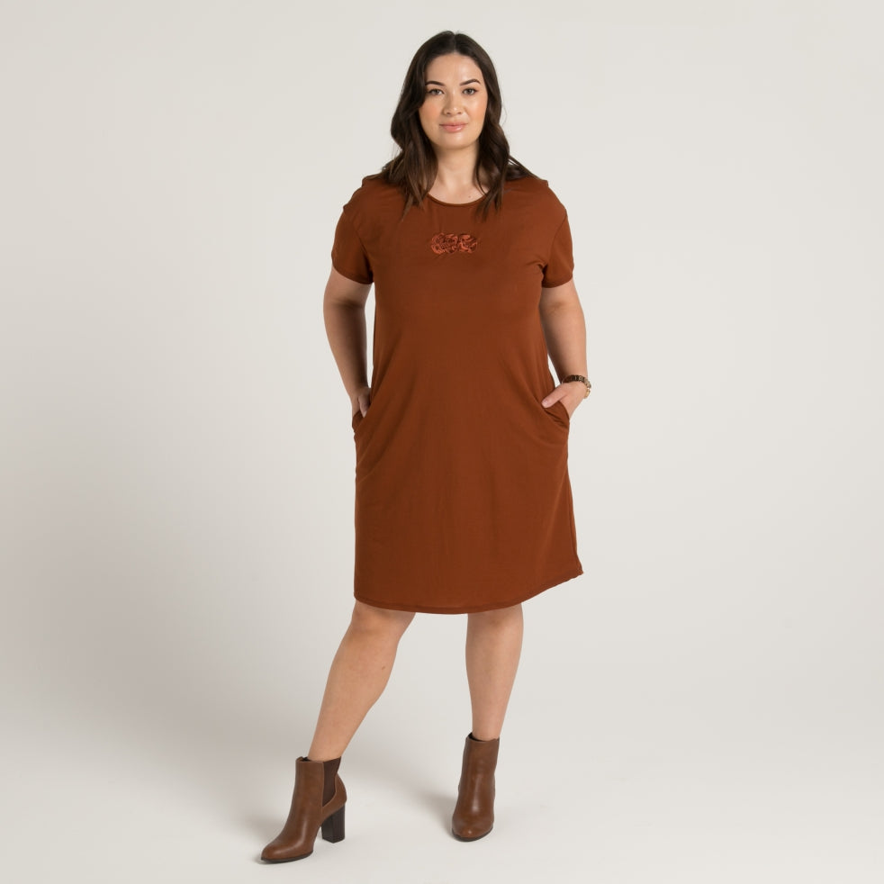 Women's brown dress with stunning embroidered maori tiki, dress has pockets and drop hem front and rear. Made in Aotearoa Tauranga New Zealand.  