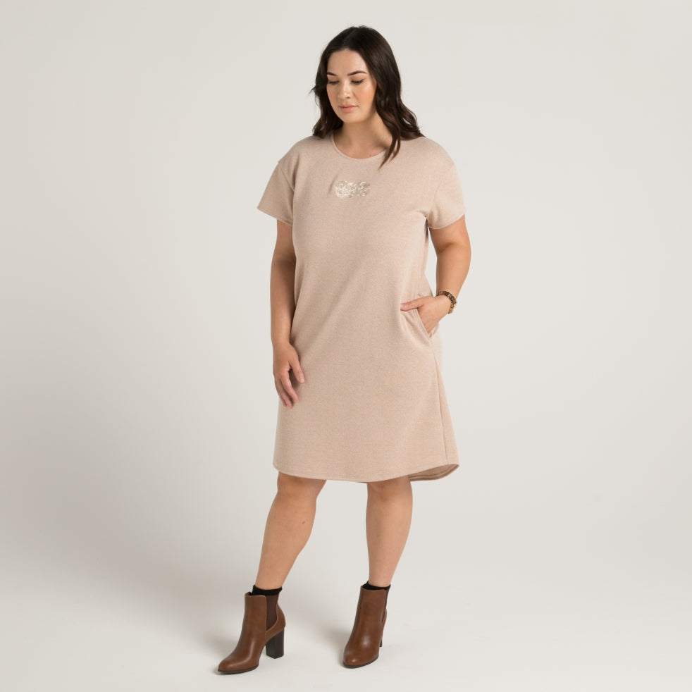 Women's textured tan dress with stunning embroidered maori tiki, dress has pockets and drop hem front and rear. Made in Aotearoa Tauranga New Zealand.